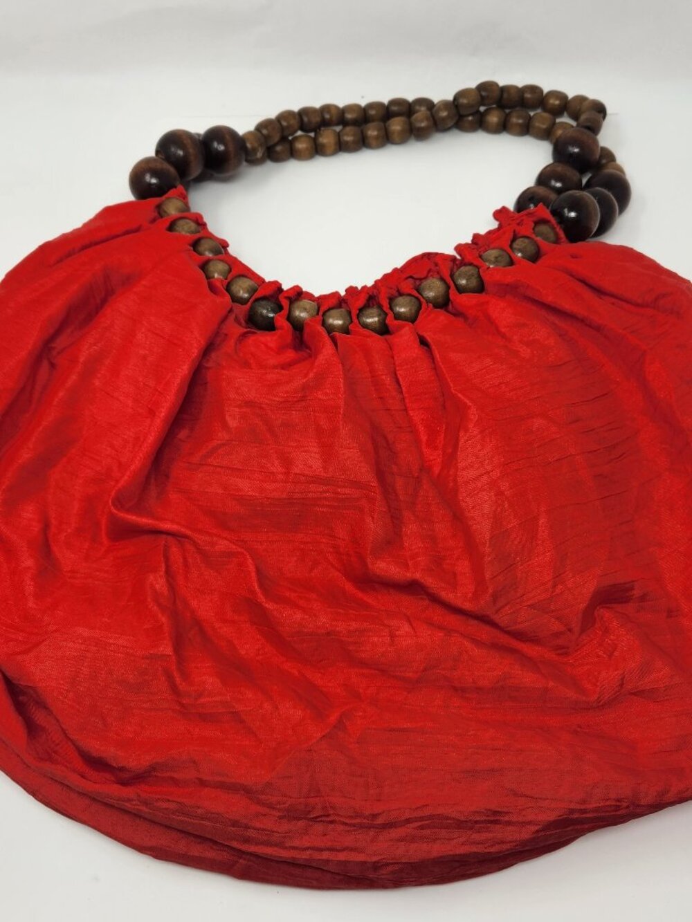 New red sling cloth handbag with light brown beads and a dark brown bead handle.